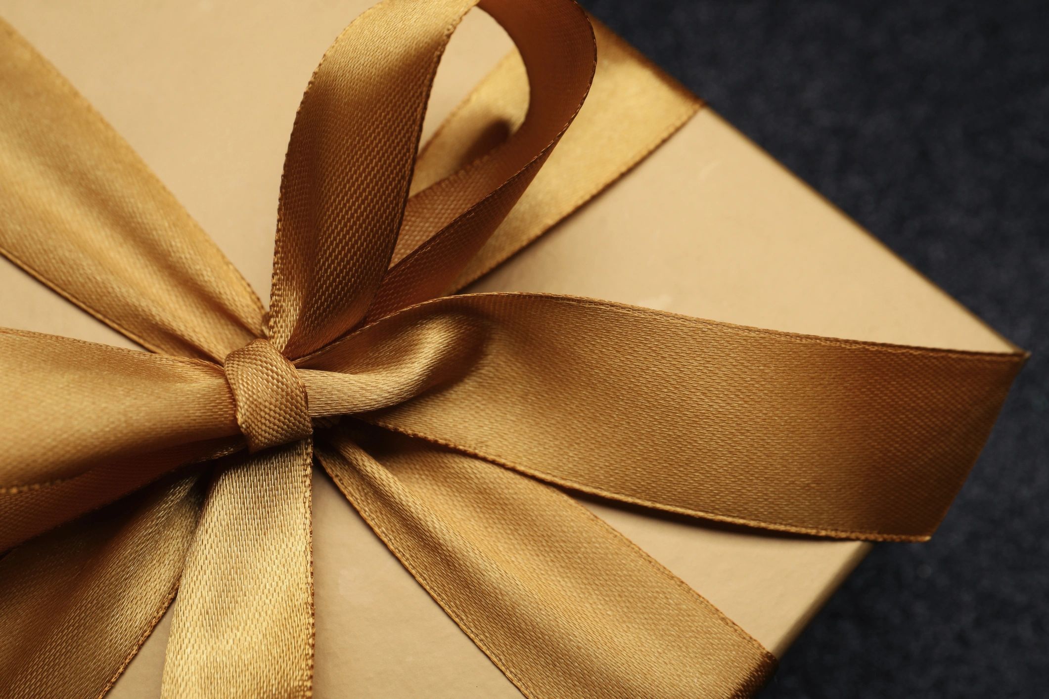 Golden gift box with satin bow on black background